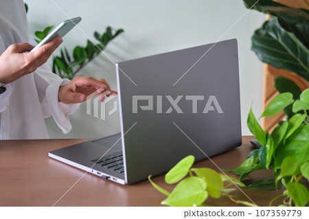 Women's hands at a laptop against a background of greenery. 107359779