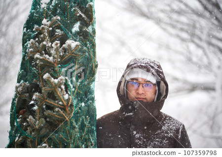 A man brought a Christmas tree into his yard during a snowstorm. 107359798