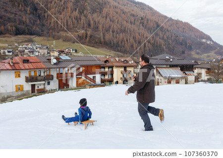 father running after his child going down the hill on sled making video on mobile phone father running after his child going down the hill on sled making video on mobile phone 107360370