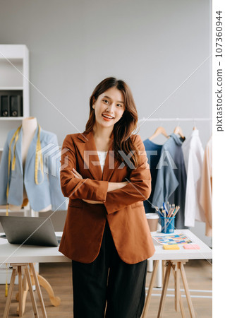 Asian young woman on desk in office of fashion designer and holds tablet, laptop and smartphone on white table Asian young woman on desk in office of fashion designer and holds tablet, laptop and smartphone on white table 107360944