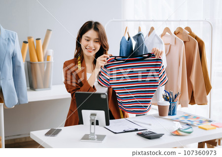 Fashion blogger concept, Young Asian women selling clothes on video streaming.Startup small business SME, using smartphone or tablet taking receive and checking. 107360973