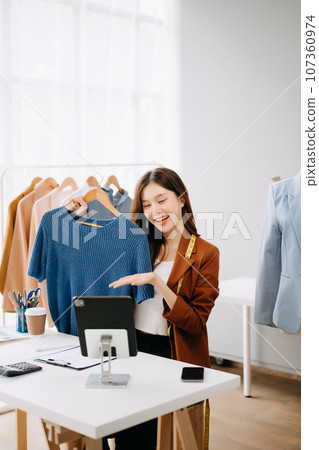 Fashion blogger concept, Young Asian women selling clothes on video streaming.Startup small business SME, using smartphone or tablet taking receive and checking. Fashion blogger concept, Young Asian women selling clothes on video streaming.Startup small business SME, using smartphone or tablet taking receive and checking. 107360974