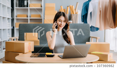 Startup small business SME, Entrepreneur owner woman using smartphone or tablet taking receive and checking online purchase shopping order to preparing pack product box. . 107360982