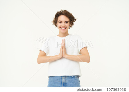 Portrait of brunette young woman holds hands together, namaste gesture, say thank you, grateful, express gratitude and joy, stands over white background 107363938