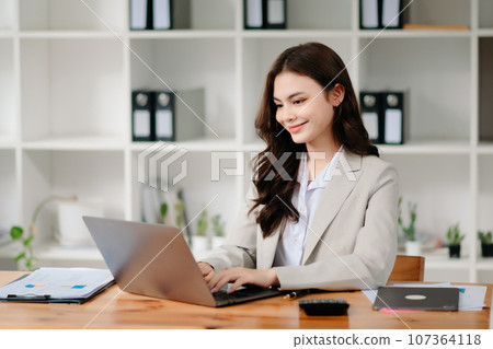 Business woman using tablet and laptop for doing math finance on an office desk, tax, report, accounting, statistics, and analytical research concept in office Business woman using tablet and laptop for doing math finance on an office desk, tax, report, accounting, statistics, and analytical research concept in office 107364118
