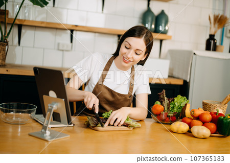 Young American woman learning online cooking class via tablet computer in kitchen 107365183