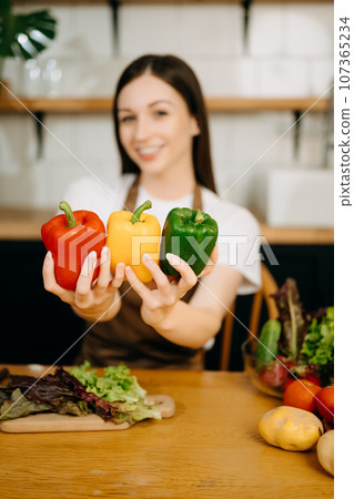 beautiful adult woman with bell peppers looking at camera while making salad at kitche. healthy food concept 107365234