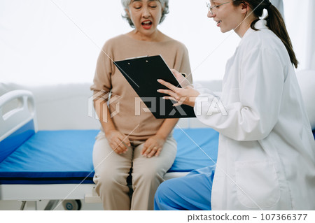 Doctor and senior  female patient who lie on the bed while checking pulse, consult and explain with nurse taking note in hospital wards or clinic.. 107366377