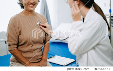 Doctor and senior female patient who lie on the bed while checking pulse, consult and explain with nurse taking note in hospital wards or clinic.. Doctor and senior female patient who lie on the bed while checking pulse, consult and explain with nurse taking note in hospital wards or clinic.. 107366457