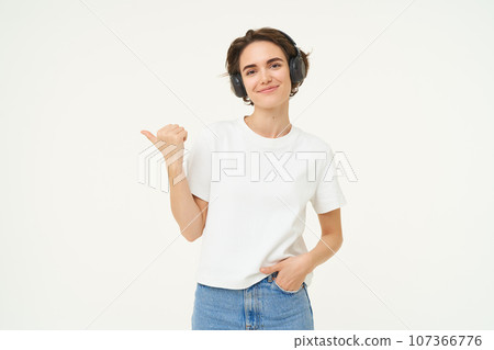 Portrait of brunette woman, smiling with confidence, pointing finger left, showing advertisement, standing over white background Portrait of brunette woman, smiling with confidence, pointing finger left, showing advertisement, standing over white background 107366776