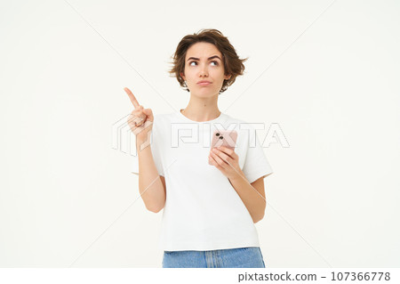 Portrait of woman thinking, using smartphone and looking thoughtful, making choice, deciding, standing isolated over white background Portrait of woman thinking, using smartphone and looking thoughtful, making choice, deciding, standing isolated over white background 107366778