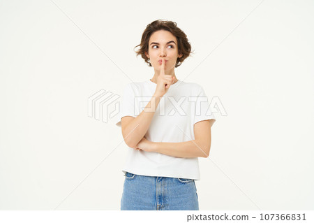 Image of brunette woman hiding secret, press finger to lips, hush, shush shh gesture, gossips, whispers, stands over white studio background 107366831