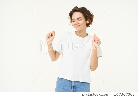 Portrait of happy young woman dancing, having fun, enjoying the music, posing over white studio background 107367063