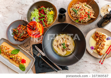 A set of Thai cuisine dishes on a table in a restaurant with a cocktail. A set of Thai cuisine dishes on a table in a restaurant with a cocktail. 107369587