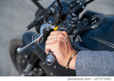 Caucasian man rides an electric motorcycle. Close-up of a man's hand pressing the gas on the steering wheel. Caucasian man rides an electric motorcycle. Close-up of a man's hand pressing the gas on the steering wheel. 107371062