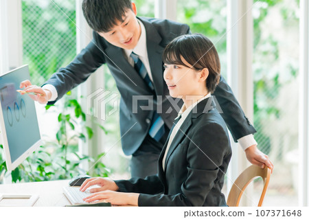 一位年輕女商人一邊看著顯示器一邊收到解釋 一位年輕女商人一邊看著顯示器一邊收到解釋 107371648