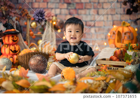 An 11-month-old baby smiles happily surrounded by a Halloween photo set in October. 107371655