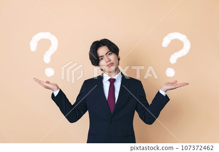 A young businessman wearing a suit who compares two things. A young businessman wearing a suit who compares two things. 107372462