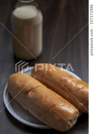 Bread on a white plate sits on a wooden board table with milk in a bottle behind it 107372986
