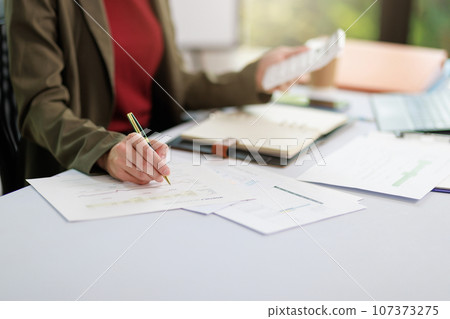 Concept of business office woman working,Businesswoman smile while working about her invesment plan with analyzing document and business investment graph data by using laptop on desk in workstation. 107373275
