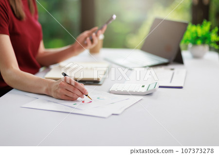 Concept of business office woman working,Businesswoman smile while working about her invesment plan with analyzing document and business investment graph data by using laptop on desk in workstation. 107373278