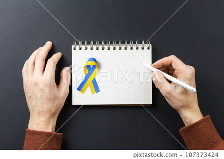 pen in my hands and yellow blue ribbon on notebook 107373424