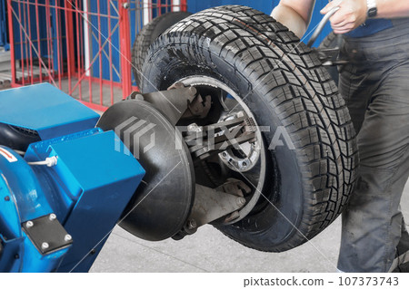 Mechanic works in tire repair shop. Car service mechanic puts wheel on car rim using special device 107373743