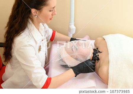 A beautician puts gauze on the patient's face A beautician puts gauze on the patient's face 107373985