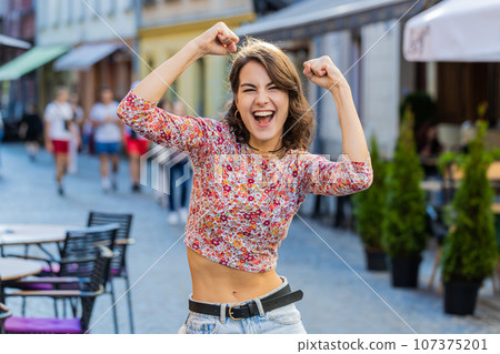 Young woman shouting, celebrating success winning goal achievement good victory news in city street Young woman shouting, celebrating success winning goal achievement good victory news in city street 107375201