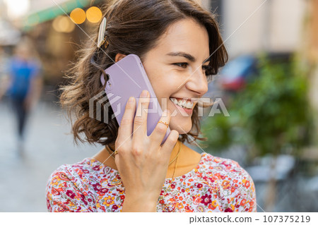 Happy young woman having remote conversation talking on smartphone, good news gossip in city street Happy young woman having remote conversation talking on smartphone, good news gossip in city street 107375219