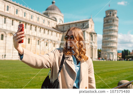 Travel tourist woman in sunglasses take a selfie at Pisa having fun posing for picture. Happy girl on Europe summer vacation taking photo at popular attraction with funny pose. 107375480