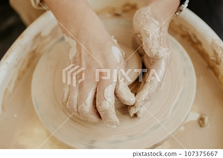 woman sculpts from clay. modeling on a potter's wheel. Hands are molded from clay. Creative workshop. The girl sculpts from clay. Working atmosphere in the workshop.  107375667