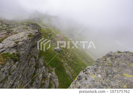 steep slopes of fagaras mountains, romania. rocks and boulders among the grass. foggy weather. mysterious adventures 107375762