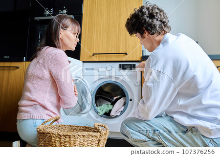 Family mother and teenage son together, at home near washing machine Family mother and teenage son together, at home near washing machine 107376256
