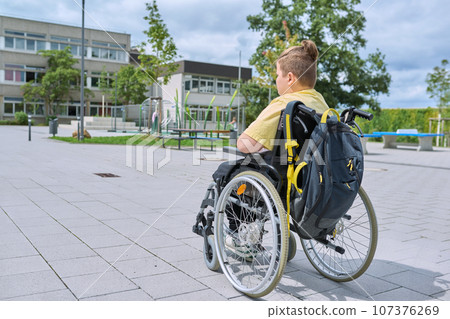 Back view, child preteen boy on wheelchair going to school building Back view, child preteen boy on wheelchair going to school building 107376269