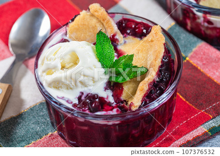 Berry cobbler in glass ramekin with ice cream, horizontal, closeup 107376532