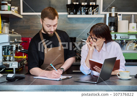 Team male and woman talking, working, using laptop, coffee shop Team male and woman talking, working, using laptop, coffee shop 107376822