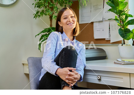 Portrait of young positive woman looking at camera, sitting on chair at home 107376828