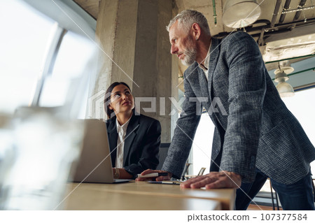 Senior male boss discussing online project with employee showing presentation to team leader Senior male boss discussing online project with employee showing presentation to team leader 107377584