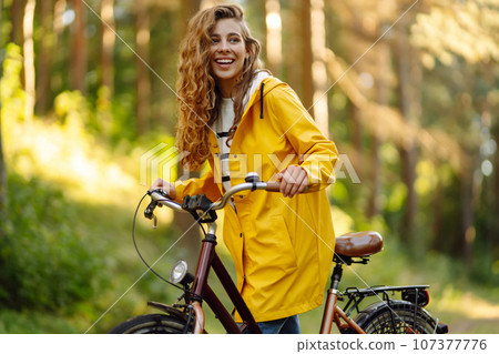 Beautiful happy woman in yellow coat riding bicycle in autumn park. Autumn fashion. Nature concept. Beautiful happy woman in yellow coat riding bicycle in autumn park. Autumn fashion. Nature concept. 107377776