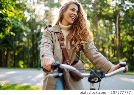 Beautiful tourist woman with curls in coat rides bicycle enjoying spring weather. Active lifestyle. Beautiful tourist woman with curls in coat rides bicycle enjoying spring weather. Active lifestyle. 107377777
