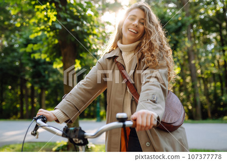Beautiful tourist woman with curls in coat rides bicycle enjoying spring weather. Active lifestyle. 107377778