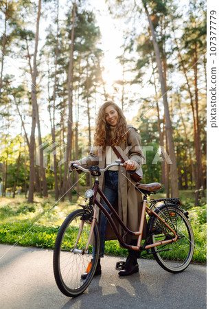Beautiful tourist woman with curls in coat rides bicycle enjoying spring weather. Active lifestyle. Beautiful tourist woman with curls in coat rides bicycle enjoying spring weather. Active lifestyle. 107377779