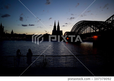 Cologne Cathedral and bridge illuminated by the setting sun 107378092