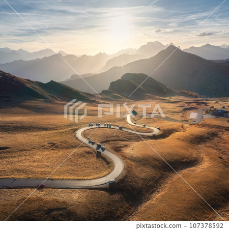 Aerial view of winding road in mountain pass, golden sunlight Aerial view of winding road in mountain pass, golden sunlight 107378592