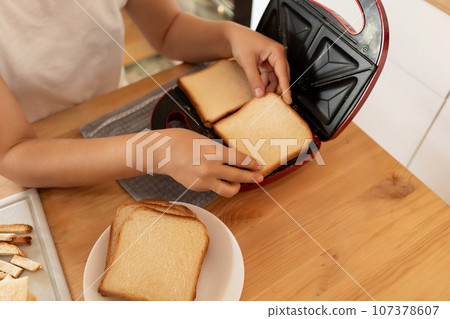a woman toasting bread in a toaster oven in her kitchen a woman toasting bread in a toaster oven in her kitchen 107378607