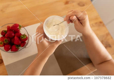 women's hands make a dessert of sour cream and strawberries 107378682
