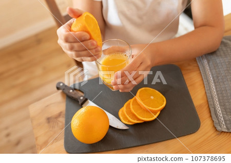a woman's hands holding a juicy orange sitting in the kitchen 107378695