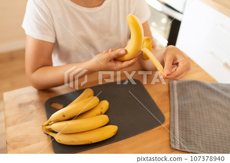 a woman peels a banana to make breakfast 107378940