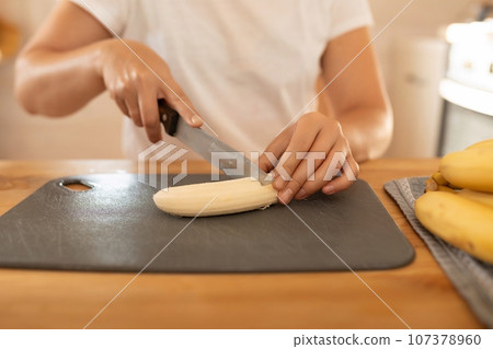 a woman slices a banana with a knife on a board in the kitchen a woman slices a banana with a knife on a board in the kitchen 107378960